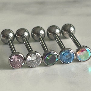 May include: Five silver barbell body jewelry pieces with different colored gems. The gems are pink, clear, iridescent, blue, and light blue.