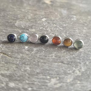 Peut inclure: Une collection de sept boucles d'oreilles à clous en pierres précieuses. Chaque boucle d'oreille présente une pierre précieuse ronde de couleur différente sertie dans une lunette argentée. Les pierres précieuses comprennent le bleu foncé, le turquoise, le rose, le noir, l'orange, le jaune et le vert.