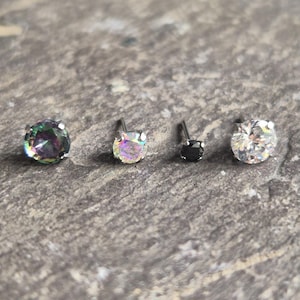 May include: Four stud earrings with various gemstones. The gemstones include an iridescent green and purple stone, a clear iridescent stone, a black stone, and a clear white stone. The earrings are set on silver posts.