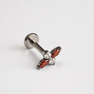 May include: A silver-toned metal labret stud featuring a flower-shaped decorative end. The flower design consists of two marquise-cut deep red stones and two round-cut clear stones arranged in an alternating pattern around a central point.