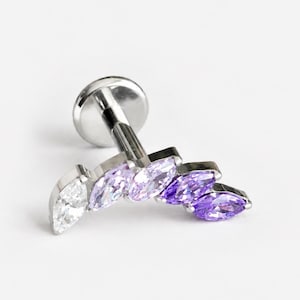 May include: A silver-toned flat back labret stud featuring a curved row of five marquise-cut gemstones. The stones transition in colour from a clear white on the left to light lavender, and finally to a deep vibrant purple on the right side.