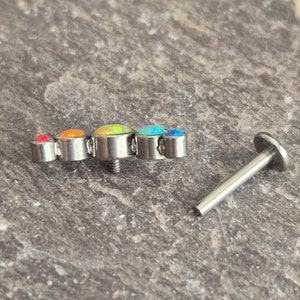 May include: A silver-toned metal body jewellery piece featuring a curved row of five round, multi-coloured cabochon stones in shades of red, orange, yellow, and blue, accompanied by a separate flat-backed metal post with a threaded end.