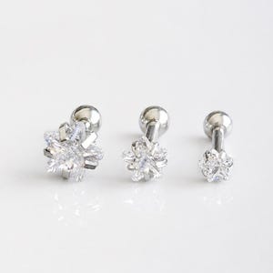 May include: Three silver-toned barbell earrings featuring star-shaped clear cubic zirconia stones in varying sizes. Each earring has a smooth metal post and a round ball backing, arranged in a row from the largest to the smallest star design.
