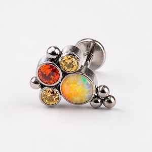 May include: A cluster-style flat back stud earring featuring a large central iridescent opal, a vibrant orange gemstone, two smaller yellow gemstones, and several polished silver-toned metal spheres arranged in a decorative, asymmetrical pattern.