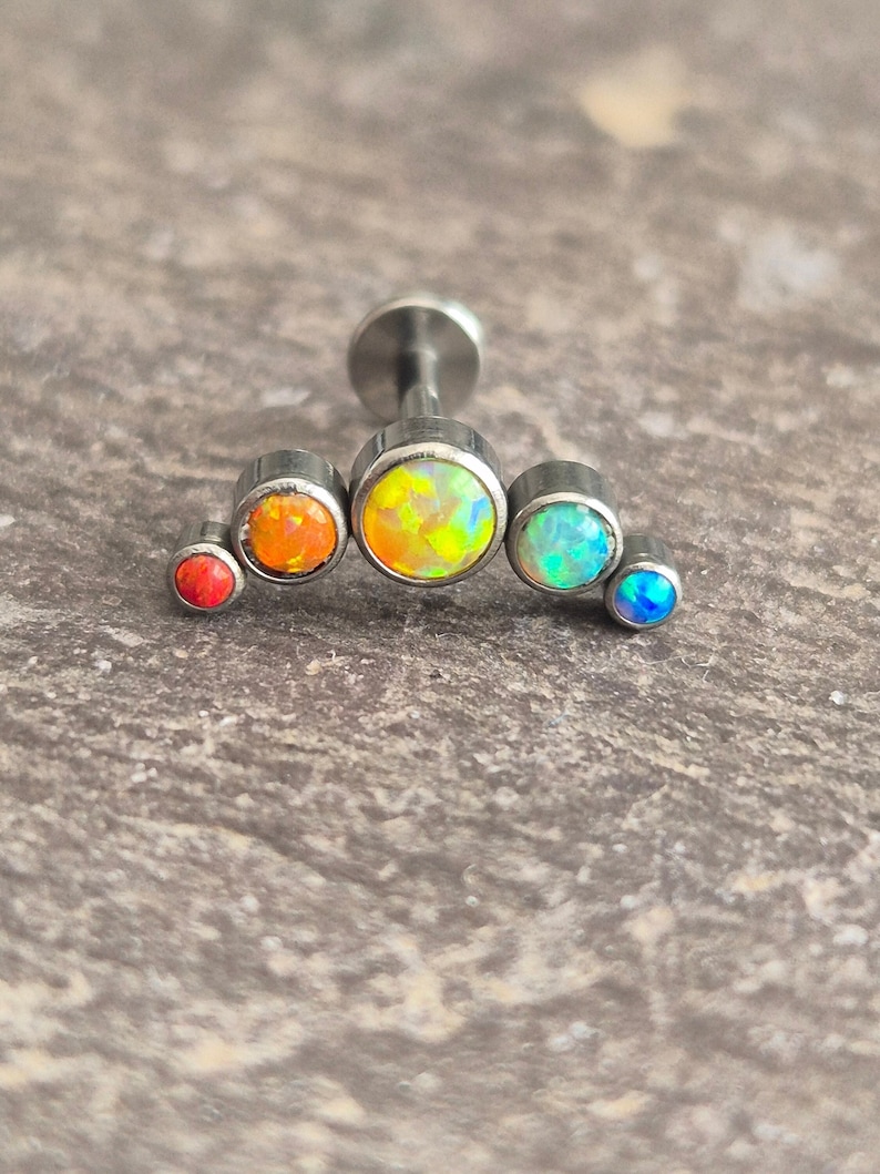 May include: A rainbow opal cartilage earring with a silver post and five opal stones in different colours, including red, orange, yellow, green, and blue.