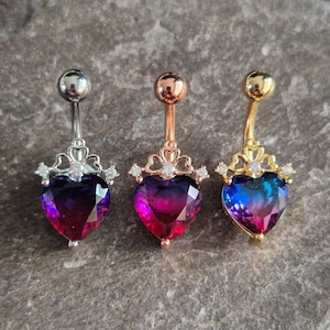May include: Three belly button rings with a heart-shaped gem. The gems are a gradient of purple, pink, and blue. Each ring has a crown-like design with small clear stones.