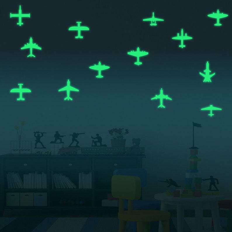 K&ouml;nnte beinhalten: Eine dunkelgr&uuml;ne Wand mit leuchtenden Flugzeugaufklebern. Die Aufkleber sind in verschiedenen Gr&ouml;&szlig;en und Positionen angebracht. Im Raum befinden sich ein B&uuml;cherregal und ein Stuhl.