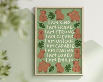May include: A rectangular wall print in a light wooden frame featuring a green background with brown capybara illustrations and green monstera leaves. The text reads: I AM KIND, I AM BRAVE, I AM STRONG, I AM CLEVER, I AM UNIQUE, I AM CAPABLE, I AM CARING, I AM LOVED, I AM EMILIO.