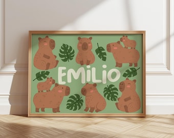 May include: A framed rectangular print with a light green background featuring brown capybara illustrations, dark green monstera leaves, and the name EMILIO written in large, bold, white, rounded capital letters in the center.