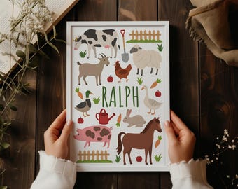 May include: A white framed print featuring the name RALPH in green letters surrounded by illustrations of a cow, goat, chicken, sheep, duck, goose, rabbit, pig, horse, shovel, fence, carrots, and apples on a white background.