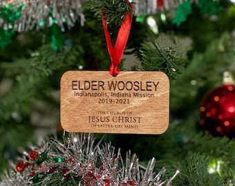 Puede incluir: Un adorno navideño de madera con el texto "ELDER WOOSLEY Indianapolis, Indiana Mission 2019-2021 THE CHURCH OF JESUS CHRIST OF LATTER-DAY SAINTS" grabado en él.