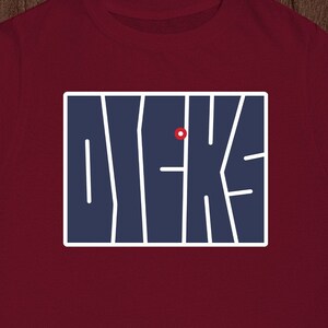 May include: A maroon t-shirt with a navy blue graphic of the word "DYKE" in a stylized font.