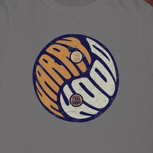 May include: Gray t-shirt with a yin yang symbol design. The symbol is in orange and blue with the words "Feel Good" and "Try New" inside.