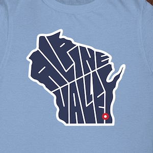 May include: Light blue t-shirt with a navy blue outline of the state of Wisconsin. The outline is filled with the words "Alpine Valley" in a stylized font.