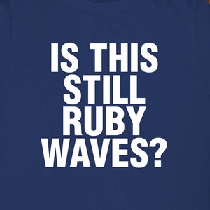 May include: A navy blue t-shirt with white text that reads "Is this still Ruby Waves?"