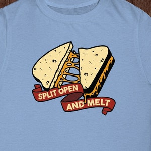 May include: A light blue t-shirt with a cartoon illustration of a split open grilled cheese sandwich with the text "SPLIT OPEN AND MELT" on a red banner.