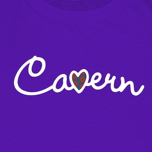 May include: Purple t-shirt with white cursive text that says "Cavern" with a heart in the middle of the word. The heart is blue with a red and white pattern.
