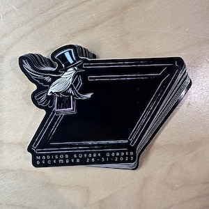 May include: A black and white sticker with a bird wearing a top hat and the text "MADISON SQUARE GARDEN DECEMBER 28-31, 2023".