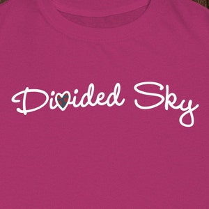 May include: A pink t-shirt with the text "Divided Sky" in white cursive lettering. A small heart with a red, white, and blue pattern is incorporated into the word "divided".
