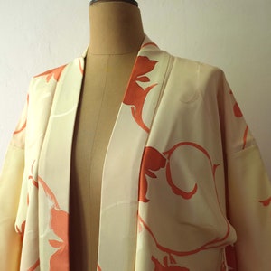 Puede incluir: Un kimono de color crema con un gran patr&oacute;n floral abstracto en tonos naranja. El kimono est&aacute; hecho de una tela sedosa y tiene un dise&ntilde;o japon&eacute;s tradicional.