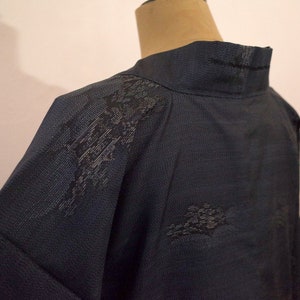 Op de afbeelding: Een donkerblauwe kimono met een zwart bloemenpatroon. De kimono heeft een hoge kraag en lange mouwen.