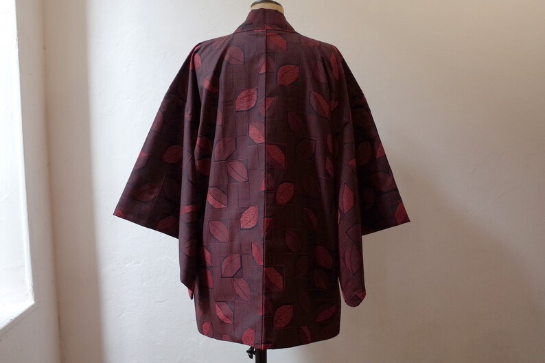 May include: A burgundy Japanese kimono with a geometric pattern of red leaves. The kimono is made of a soft, silky fabric and has a traditional design.