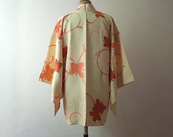 May include: A cream-colored kimono with a floral pattern in shades of orange. The kimono has a traditional Japanese design with a wide collar and long sleeves.