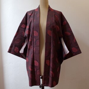 May include: A burgundy kimono with a red leaf pattern. The kimono has a white lining and is open in the front.