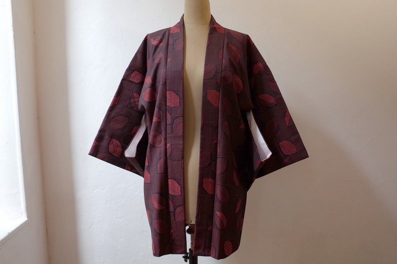 May include: A burgundy kimono with a red leaf pattern. The kimono has a white lining and is open in the front.