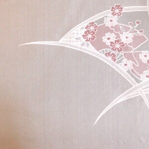 Op de afbeelding: Een witte stof met een delicaat roze bloemenpatroon. Het patroon heeft een waaiervormig ontwerp met witte lijnen en roze bloemen.