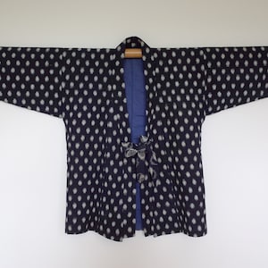 May include: A black and white polka dot kimono with a blue lining. The kimono is hanging on a wooden rod.
