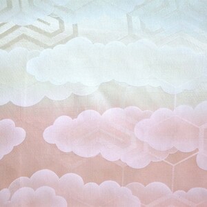 K&ouml;nnte beinhalten: Ein wei&szlig;er Stoff mit einem dezenten Muster aus Wolken und geometrischen Formen. Der Stoff hat einen Farbverlauf von Hellblau zu Rosa.