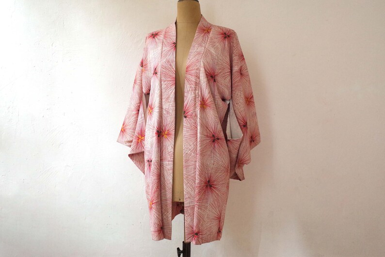 May include: A pink and white kimono with a floral pattern. The kimono has a long, flowing silhouette and is made of a lightweight fabric.