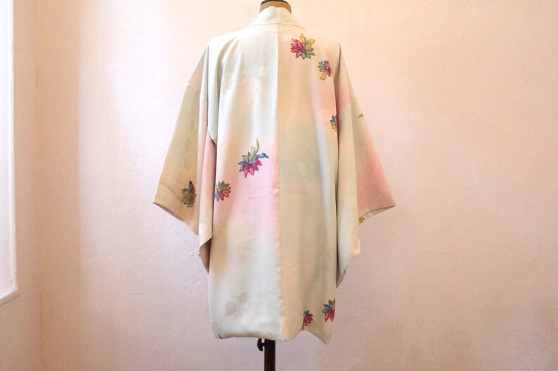 K&ouml;nnte beinhalten: Ein hellgr&uuml;nes und rosa japanisches Kimono mit Blumenstickerei. Das Kimono hat ein traditionelles Design und ist aus einem weichen, flie&szlig;enden Stoff gefertigt.