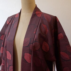 May include: A burgundy kimono with a geometric pattern of red leaves. The kimono is open in the front and has long sleeves.