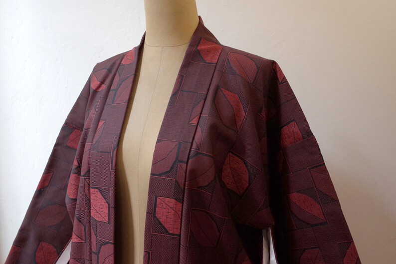 May include: A burgundy kimono with a geometric pattern of red leaves. The kimono is open in the front and has long sleeves.