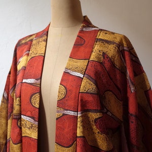 May include: A red and gold kimono with an abstract pattern. The kimono is open in the front and has a long, flowing silhouette.