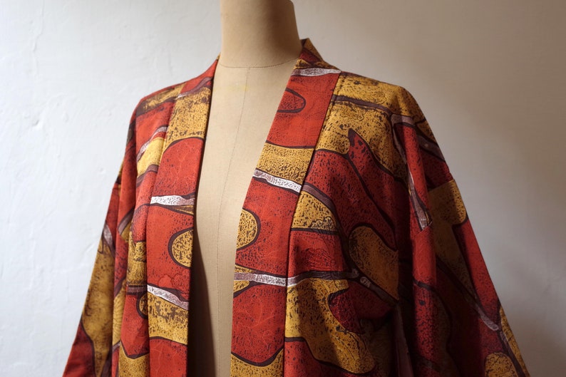 May include: A red and gold kimono with an abstract pattern. The kimono is open in the front and has a long, flowing silhouette.