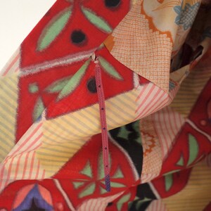 May include: A close-up of a colorful fabric with a geometric pattern. The fabric is folded over and a purple zipper is visible.