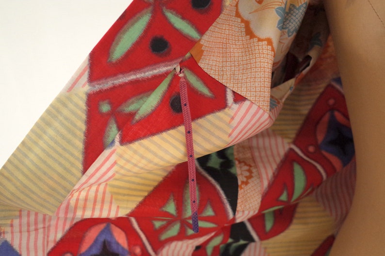 May include: A close-up of a colorful fabric with a geometric pattern. The fabric is folded over and a purple zipper is visible.