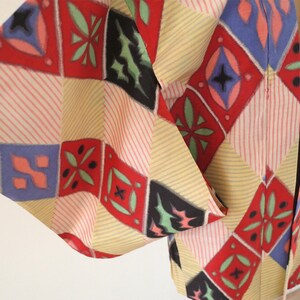 May include: A traditional Japanese haori jacket with a colorful geometric pattern in shades of red, blue, green, and yellow. The fabric is a lightweight cotton with a subtle striped texture.