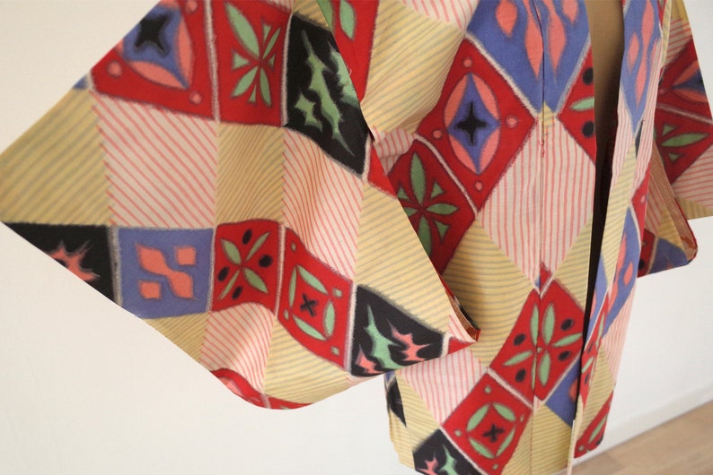 May include: A traditional Japanese haori jacket with a colorful geometric pattern in shades of red, blue, green, and yellow. The fabric is a lightweight cotton with a subtle striped texture.