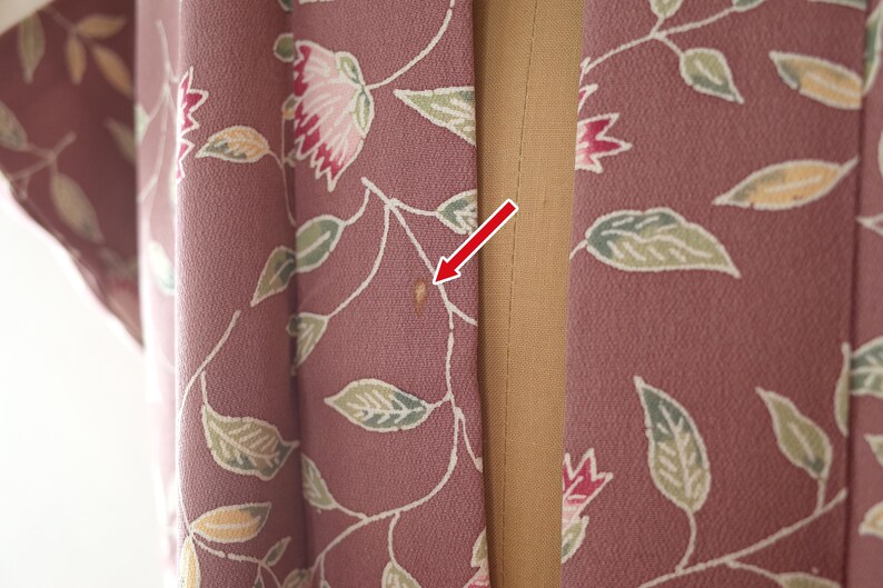 May include: A close-up of a pink fabric with a floral pattern. The fabric has a small brown stain on it.