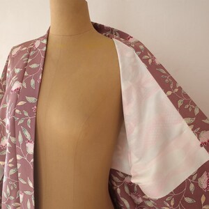 May include: A mauve kimono with a floral pattern of pink flowers and green leaves. The kimono is open to reveal a white lining.