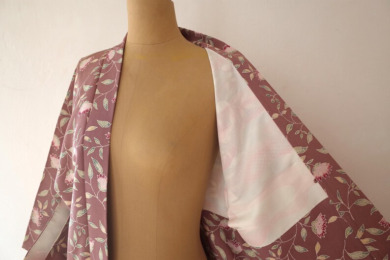 May include: A mauve kimono with a floral pattern of pink flowers and green leaves. The kimono is open to reveal a white lining.
