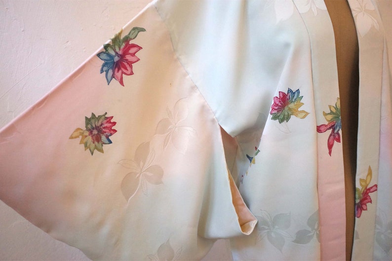 K&ouml;nnte beinhalten: Ein hellblaues und rosafarbenes Kimono mit Blumenmuster. Das Kimono hat ein rosafarbenes Futter und ist aus einem weichen, seidigen Stoff gefertigt.