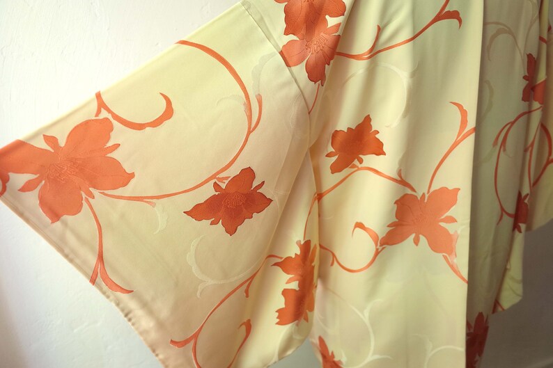 Puede incluir: Un kimono de color crema con un patr&oacute;n floral en tonos naranja. El kimono est&aacute; hecho de una tela suave y sedosa y presenta un dise&ntilde;o japon&eacute;s tradicional.
