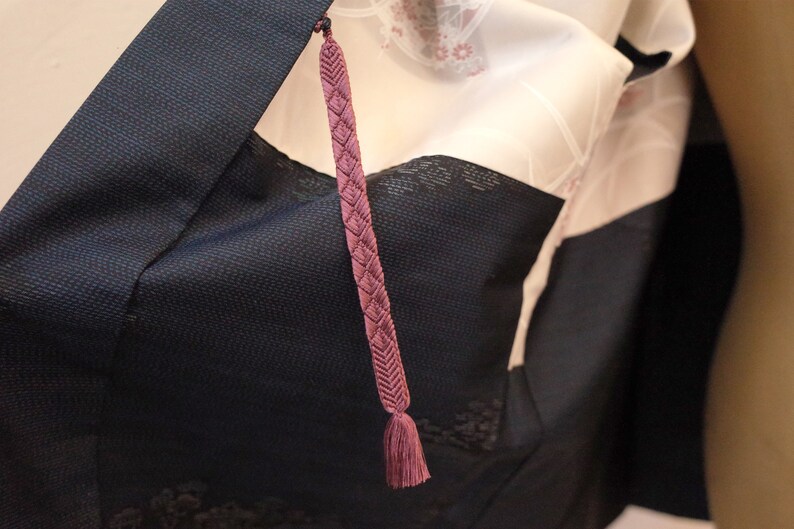 Op de afbeelding: Een close-up van een donkerblauwe kimono met een roze kwast die aan de kraag hangt.
