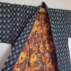 May include: A blue and white checkered kimono with a floral lining. The kimono is open and hanging on a wooden hanger.