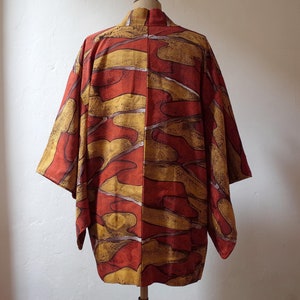 May include: A red and gold Japanese kimono with an abstract pattern. The kimono is made of a soft, flowing fabric and has a relaxed fit.